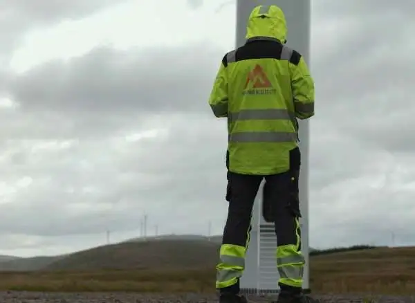A technician in high-visibility clothing looking up at the base of a wind turbine